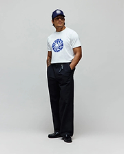 Mens Toby Graphic Tee, a white jersey t-shirt with a large blue Psycho Bunny circular graphic on the chest, paired with relaxed black pants and a navy cap featuring a white embroidered bunny skull. (3)