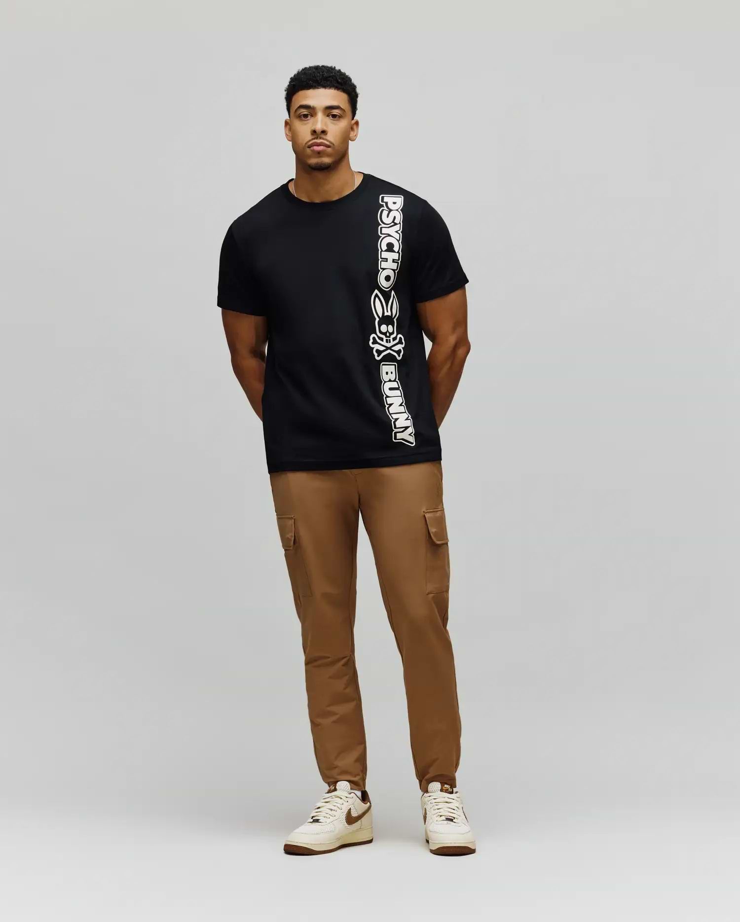 Mens Toby Wordmark Tee, a classic fit black jersey t-shirt featuring a large, vertical white Psycho Bunny wordmark and iconic bunny skull logo on the left side. (4)