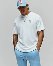 Mens Ara Oversized Tee in white jersey with a small, colorful deconstructed Psycho Bunny logo on the left chest, paired with light blue french terry sweatpants featuring an embroidered tone-on-tone logo on the left thigh. (3)