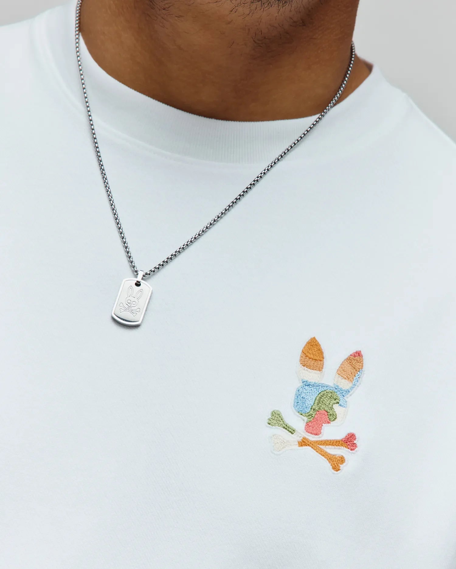 Mens Ara Oversized Tee, a premium white jersey knit t-shirt with a relaxed fit, showcasing a vibrant, multicolored embroidered Psycho Bunny skull logo on the left chest. (2)