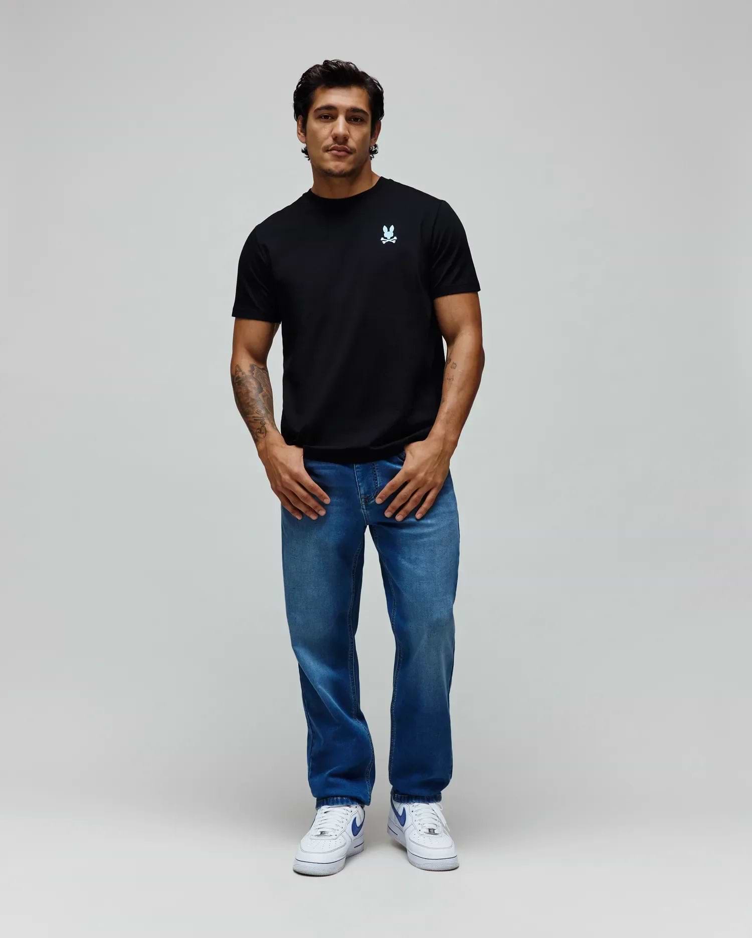 Black Mens Aiden Back Graphic Tee in classic fit jersey with a small light blue embroidered Psycho Bunny skull logo on the left chest, paired with relaxed fit medium wash blue denim jeans. (4)