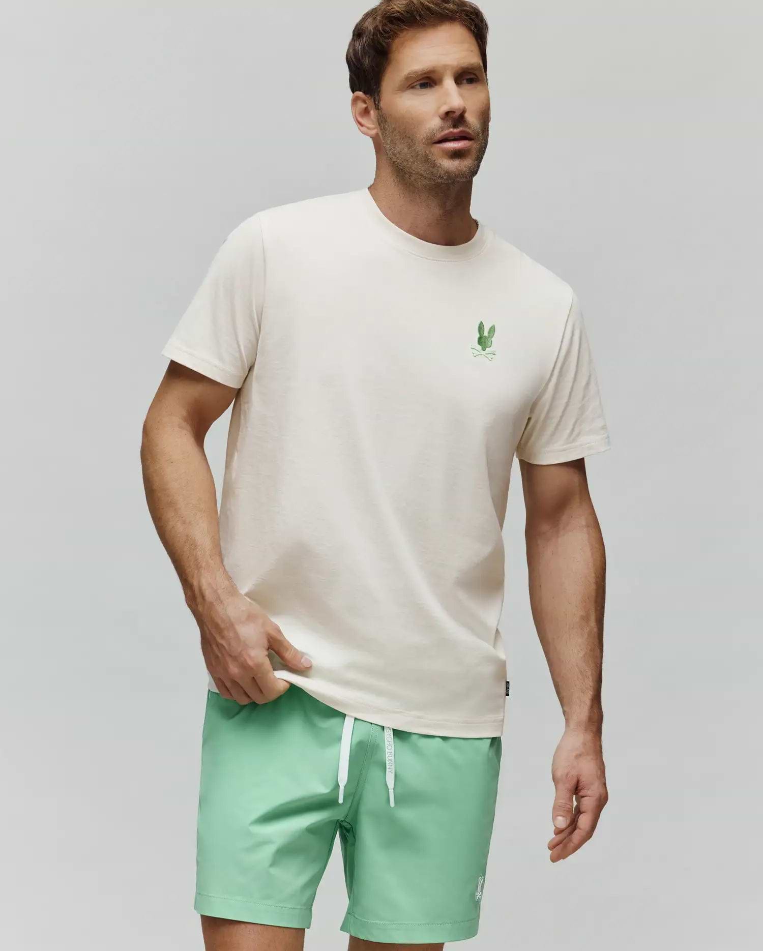 MENS AIDEN BACK GRAPHIC TEE in cream, crafted from soft jersey knit cotton with a classic fit. Features a small, vibrant green embroidered Psycho Bunny skull logo on the left chest and an implied back graphic. (3)