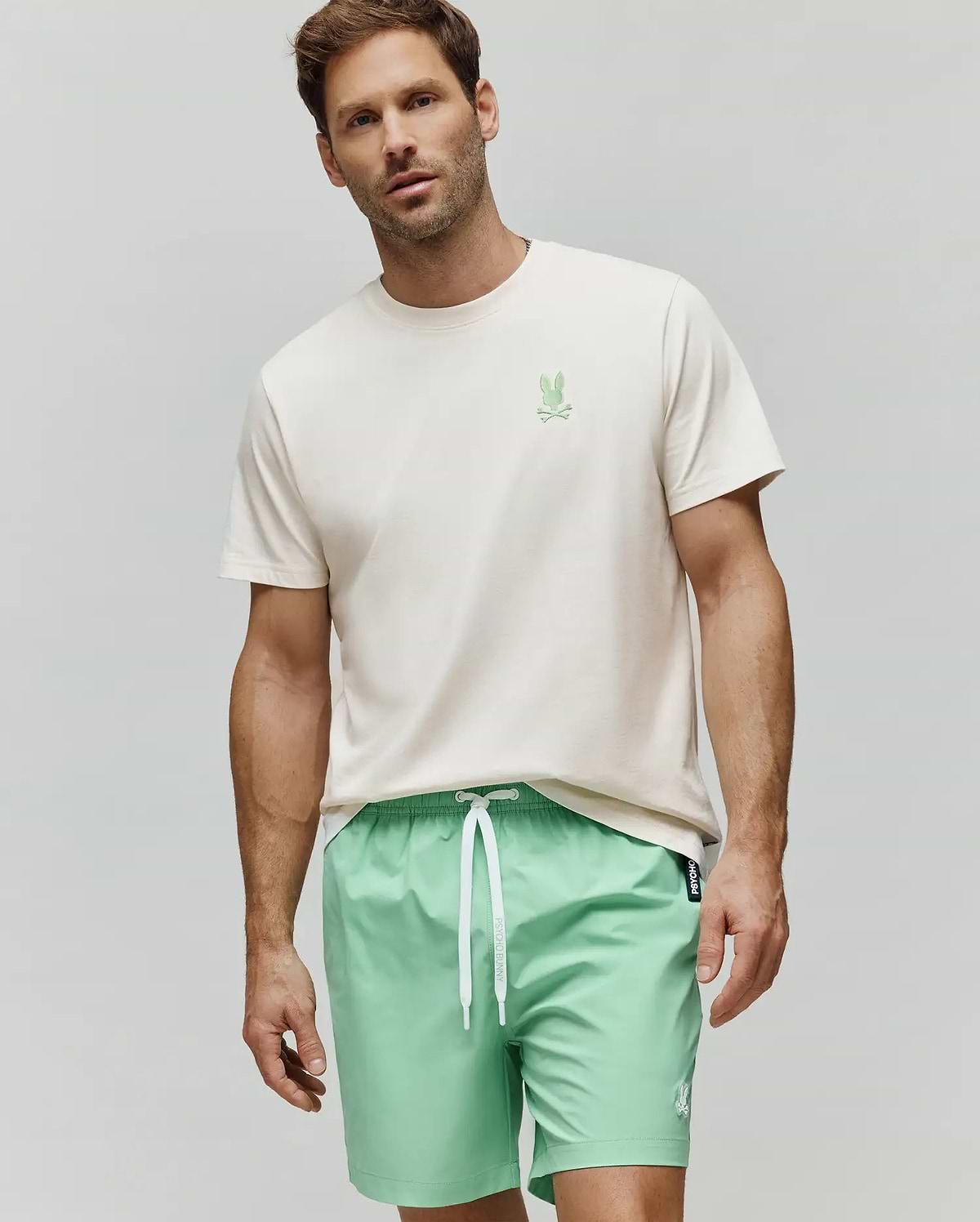 Mens Aiden Back Graphic Tee, a cream jersey t-shirt with a small green embroidered Psycho Bunny chest logo, and mint green swim shorts with a white drawstring and small white embroidered bunny logo. (2)