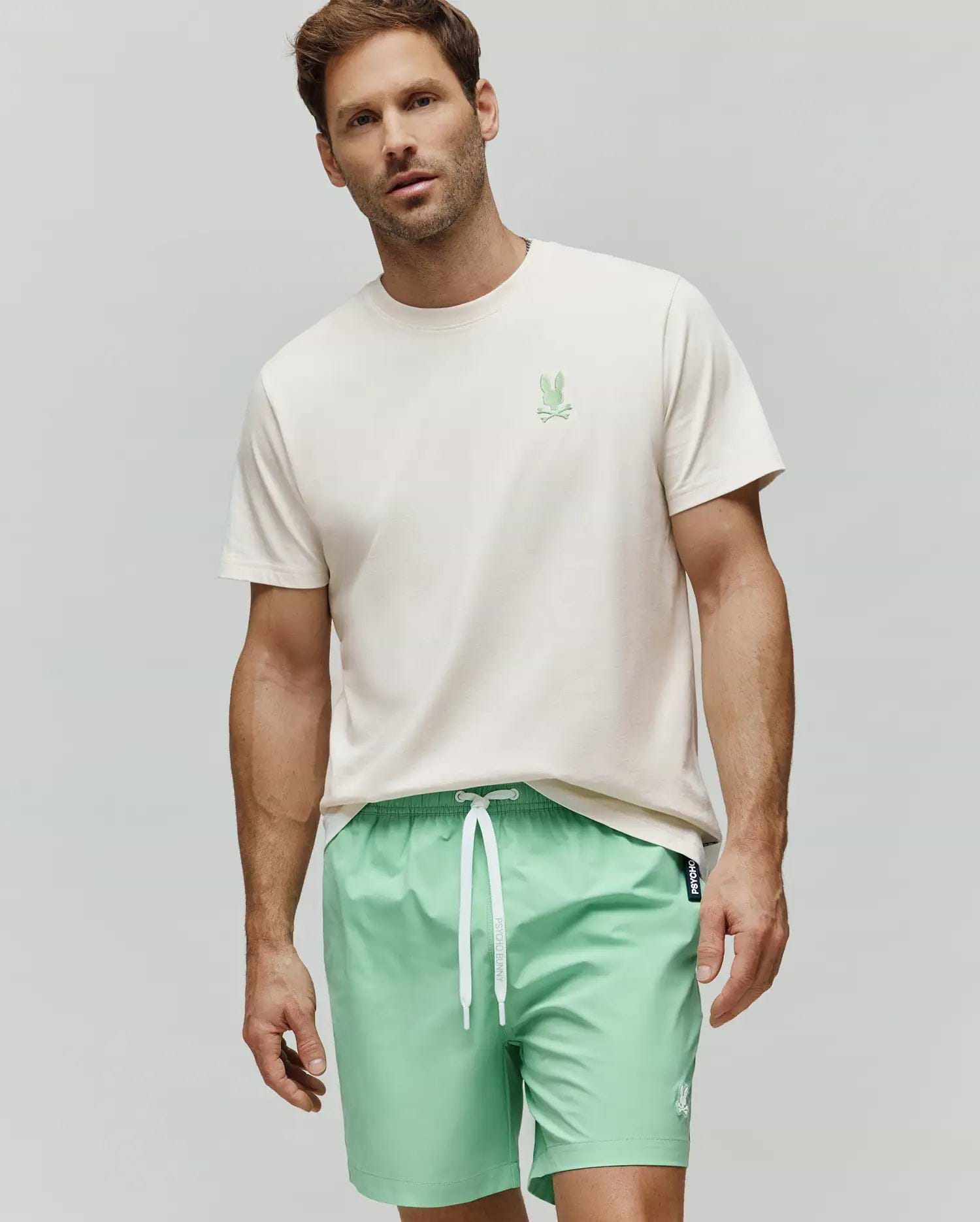 Mens Aiden Back Graphic Tee, a cream jersey t-shirt with a small green embroidered Psycho Bunny chest logo, and mint green swim shorts with a white drawstring and small white embroidered bunny logo. (2)