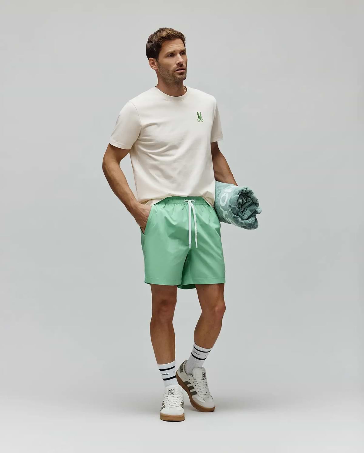 Cream Mens Aiden Back Graphic Tee, a classic fit jersey tee with a small green embroidered Psycho Bunny skull logo on the left chest, styled with relaxed mint green drawstring shorts. (4)