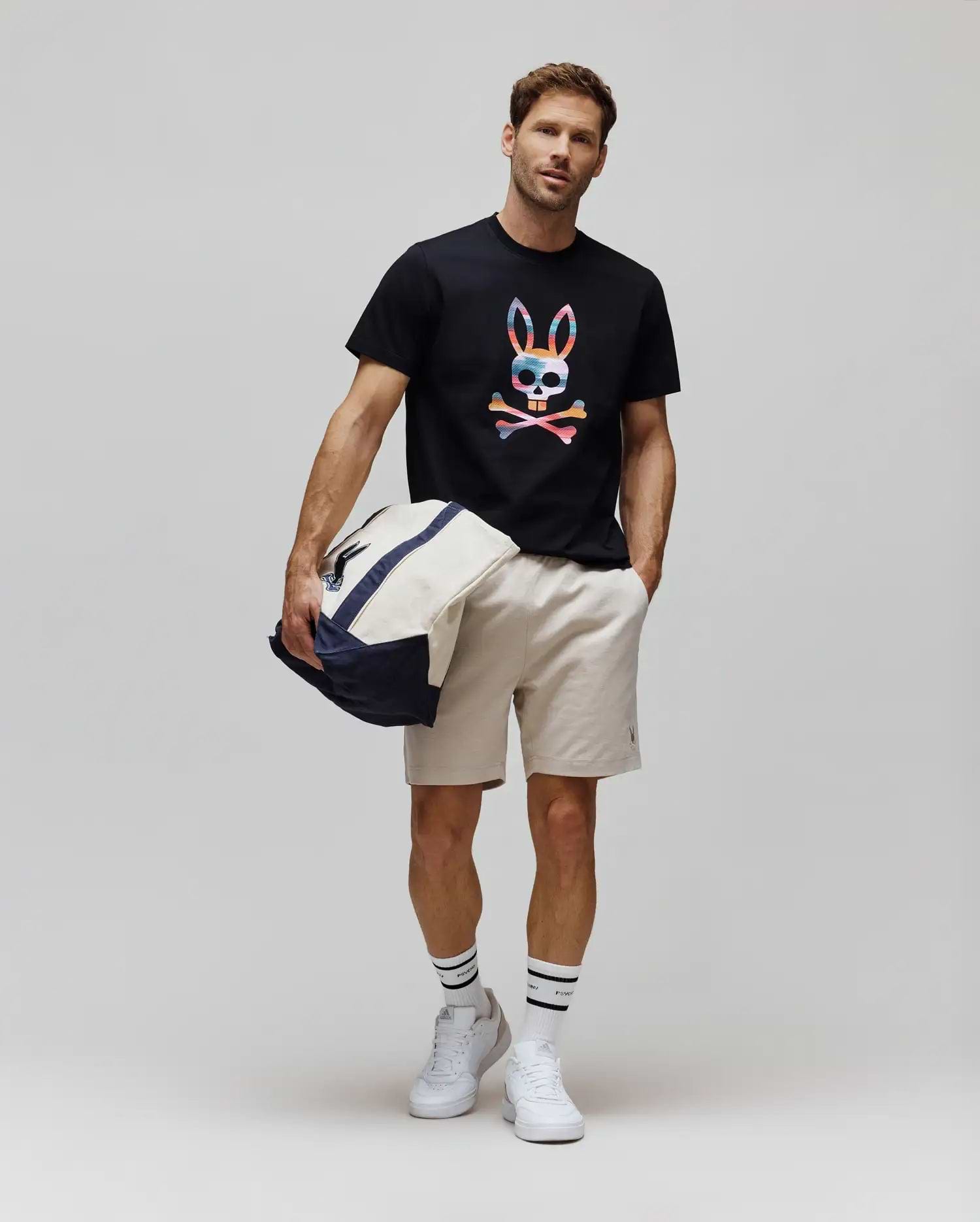 Black Mens Raphael Graphic Tee, a classic fit jersey t-shirt featuring a large, vibrant multicolor striped Psycho Bunny skull chest graphic, paired with beige woven shorts detailed with a small embroidered bunny logo. (5)