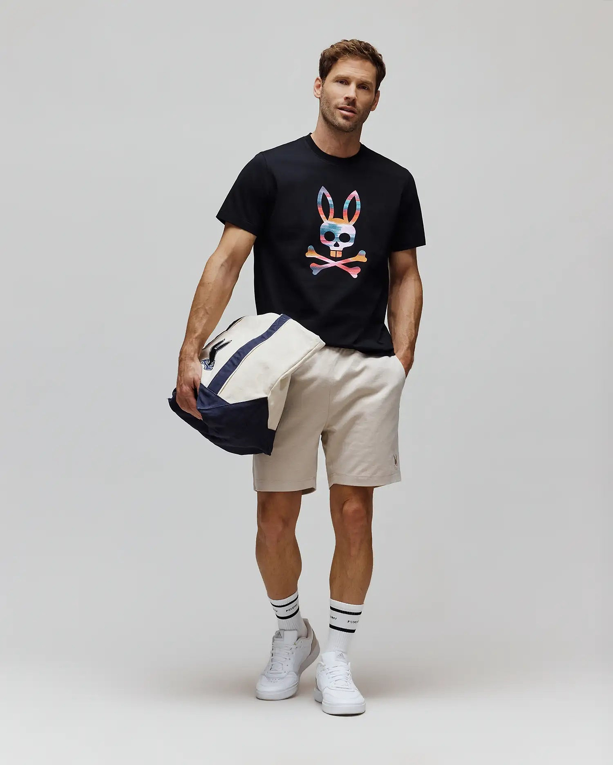 Black Mens Raphael Graphic Tee, a classic fit jersey t-shirt featuring a large, vibrant multicolor striped Psycho Bunny skull chest graphic, paired with beige woven shorts detailed with a small embroidered bunny logo. (5)