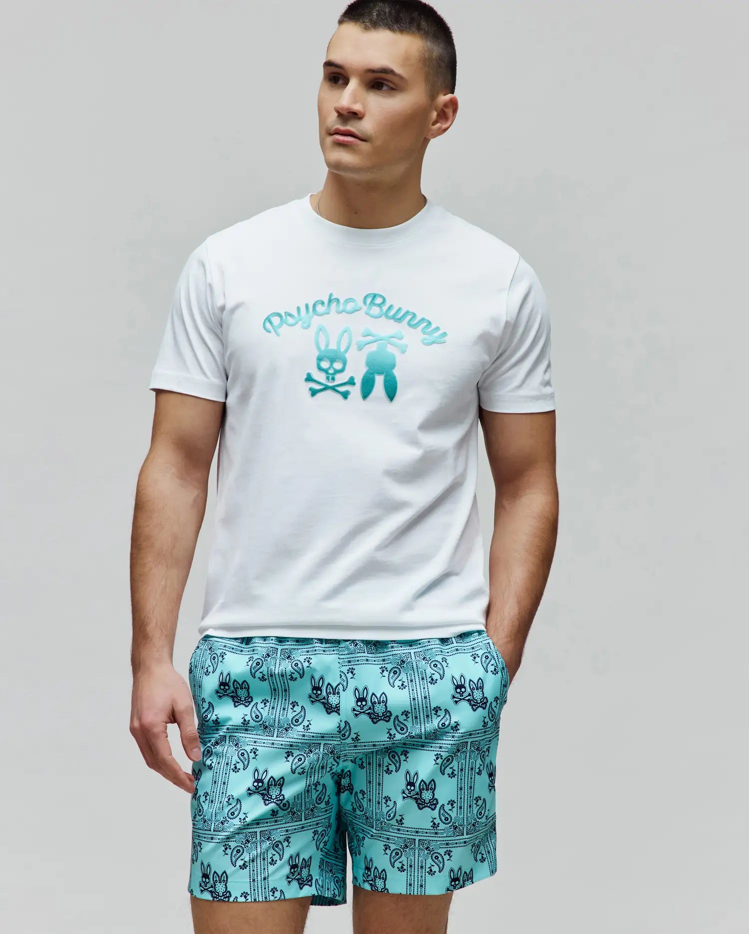 Mens Aram Graphic Tee in classic fit white jersey, featuring a large central chest graphic with Psycho Bunny script, the iconic bunny skull, and bunny tail elements in a vibrant teal gradient. (2)