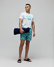 Mens Aram Graphic Tee, white jersey with a large teal gradient Psycho Bunny skull logo, paired with teal bandana print swim shorts featuring small bunny skulls, and black logo slides. (4)