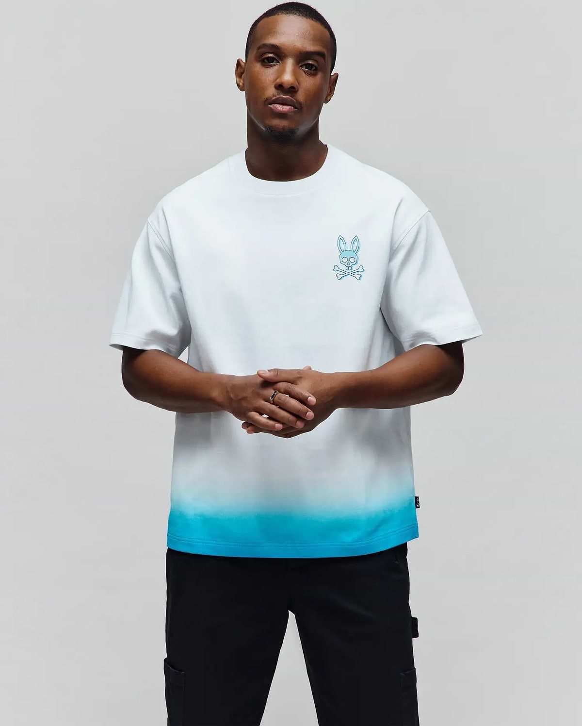 Mens Dax Oversized Tee, a white jersey t-shirt with an oversized fit, featuring a vibrant blue ombre fade at the hem and a small embroidered Psycho Bunny skull logo on the left chest. (1)