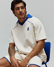 Mens Toby Jersey: Relaxed cream jersey polo with royal blue spread collar, V-neck, piping, and small embroidered bunny skull on chest; matching shorts have royal blue trim and graphic logo. (4)