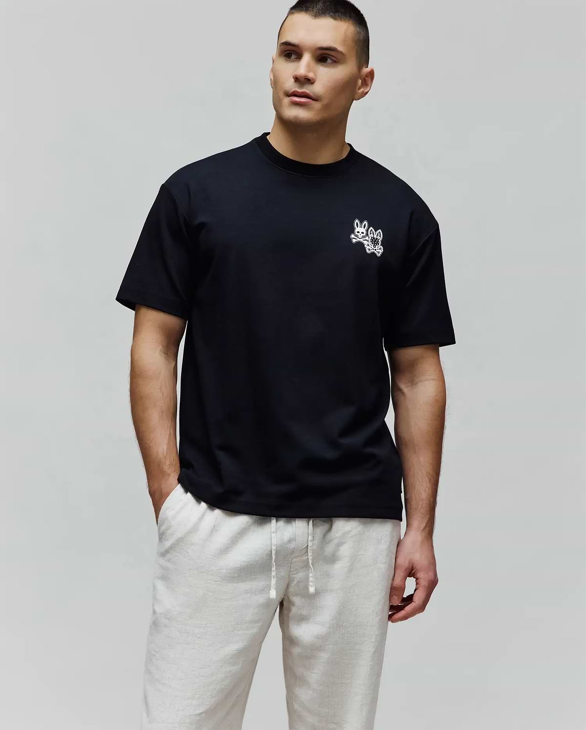 Black Mens Luke Back Graphic Tee, a relaxed fit jersey t-shirt with a small white embroidered Psycho Bunny double-bunny skull logo on the left chest and a graphic on the back.