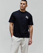 Black Mens Luke Back Graphic Tee, a relaxed fit jersey t-shirt with a small white embroidered Psycho Bunny double-bunny skull logo on the left chest and a graphic on the back.