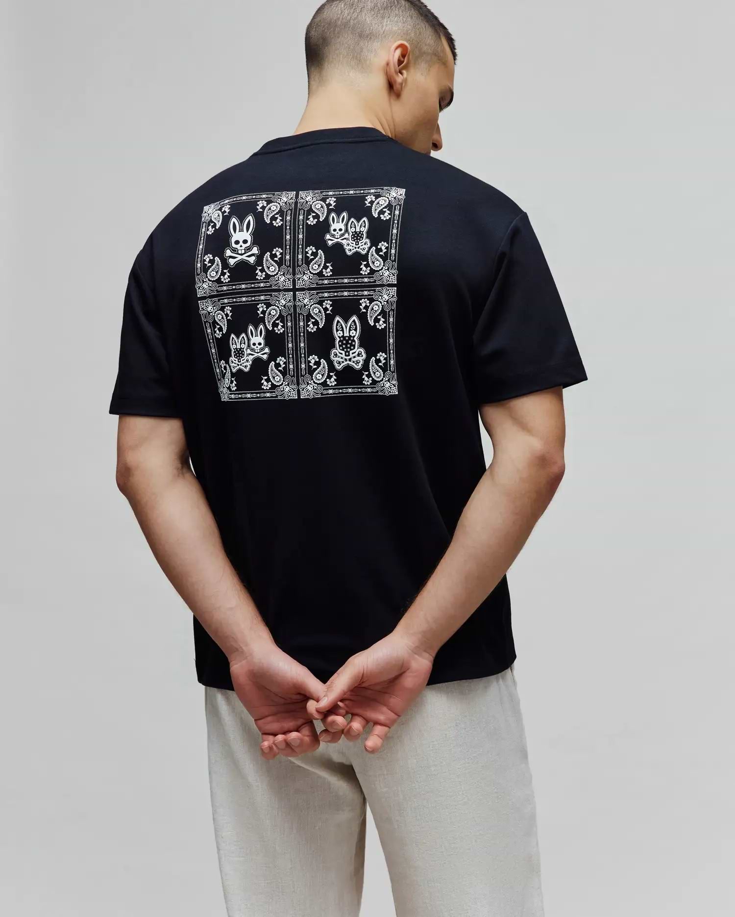 Black Mens Luke Back Graphic Tee in soft jersey, classic fit, featuring a large white bandana-style graphic on the back with four Psycho Bunny skull logos and paisley patterns.