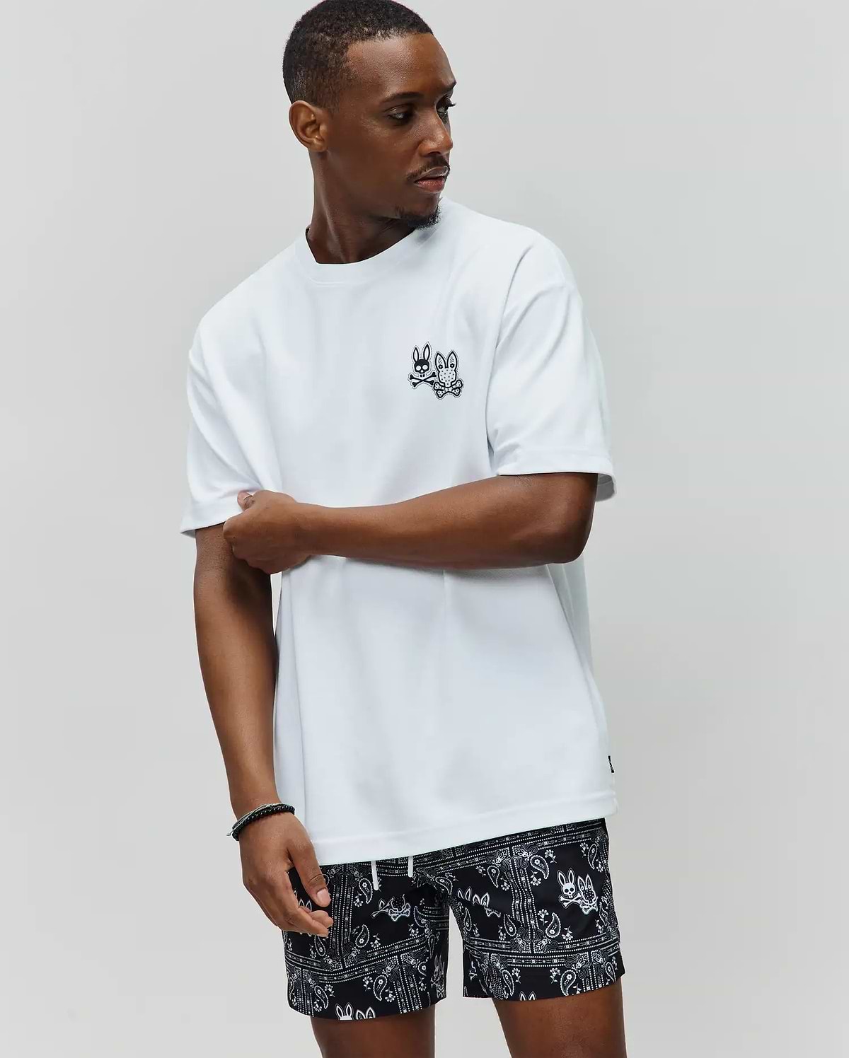 White Mens Luke Back Graphic Tee, relaxed fit, smooth jersey, with a small black embroidered Psycho Bunny skull logo on the left chest and a subtle hem tag.