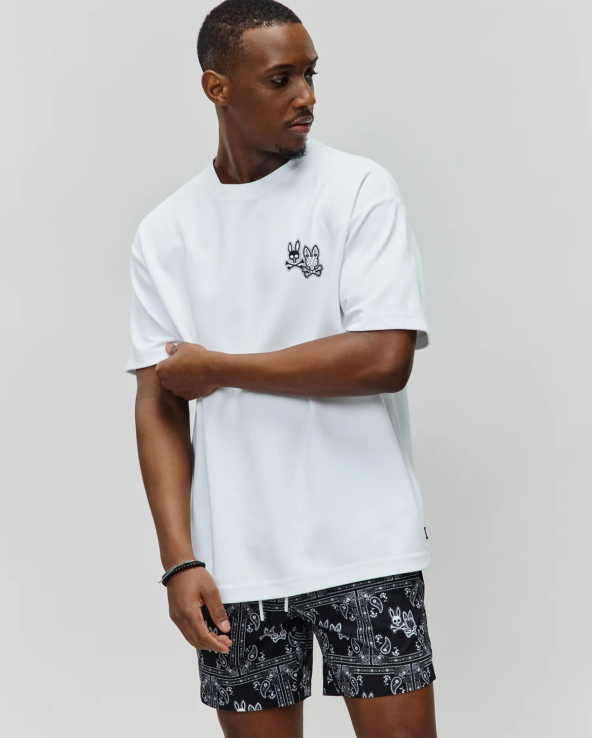 White Mens Luke Back Graphic Tee, relaxed fit, smooth jersey, with a small black embroidered Psycho Bunny skull logo on the left chest and a subtle hem tag.