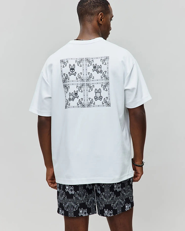 Mens Luke Back Graphic Tee. White relaxed-fit jersey t-shirt with a large black and white bandana-style back graphic featuring four Psycho Bunny skull logos. Black shorts with matching all-over white bandana and bunny skull print.