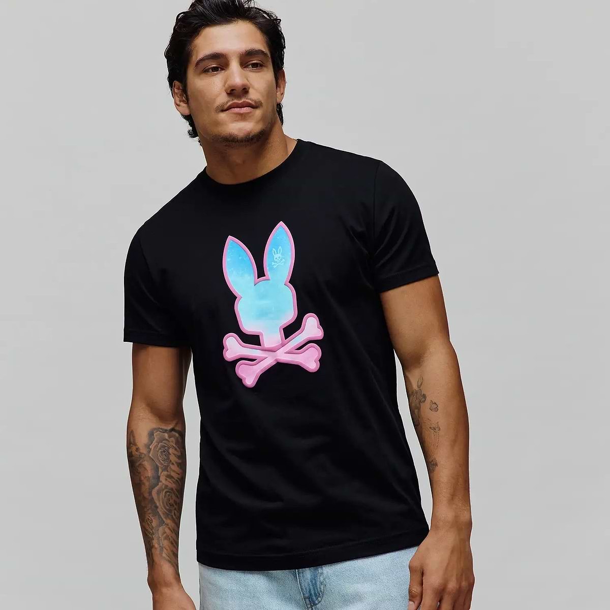 Mens Caspian Graphic Tee, a black classic fit jersey t-shirt featuring a prominent center chest graphic print of the iconic Psycho Bunny skull logo with a vibrant blue and pink gradient fill.