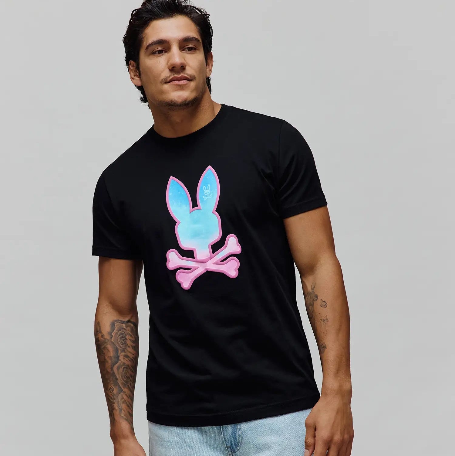 Mens Caspian Graphic Tee, a black classic fit jersey t-shirt featuring a prominent center chest graphic print of the iconic Psycho Bunny skull logo with a vibrant blue and pink gradient fill.