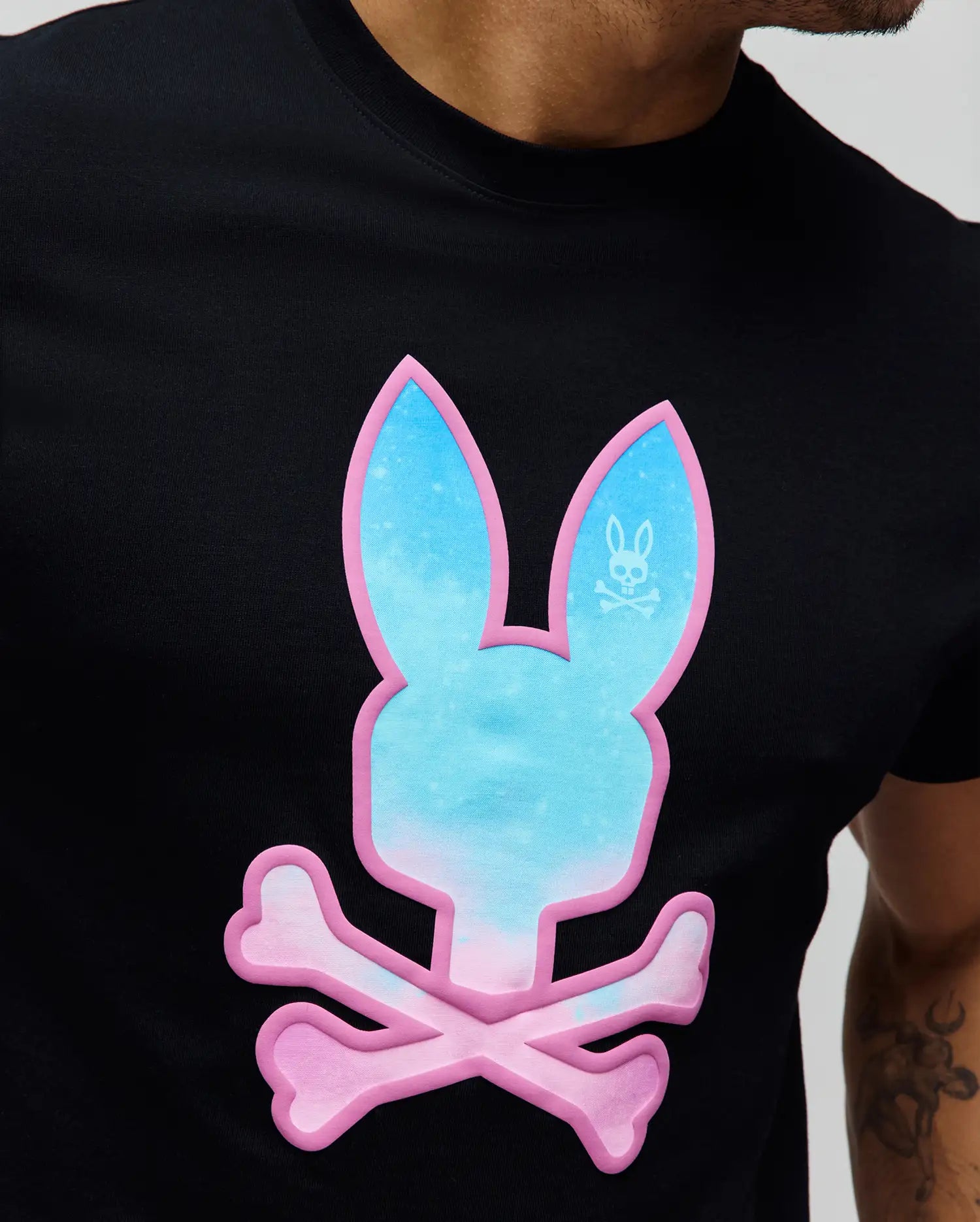 Mens Caspian Graphic Tee, black jersey t-shirt with a large, central puff print Psycho Bunny logo in a blue-to-pink gradient, outlined in vibrant pink, featuring a small white logo in the ear.