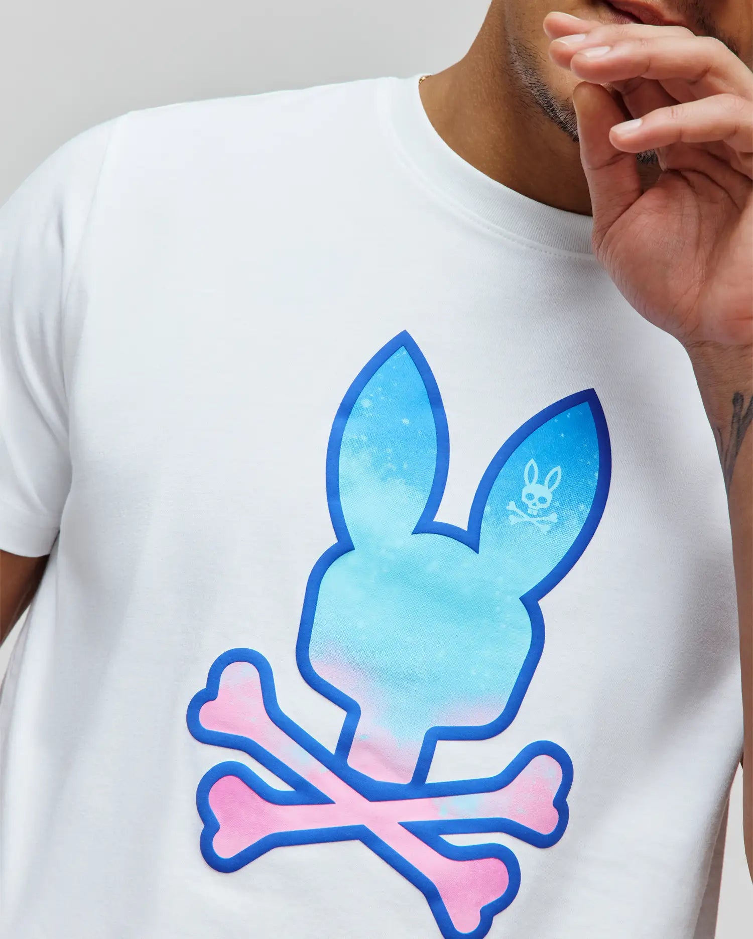 Mens Caspian Graphic Tee, white classic fit jersey t-shirt with a large central blue-to-pink gradient puffy print Psycho Bunny skull and crossbones graphic, outlined in dark blue, featuring a smaller white logo in the ear.