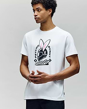 A man stands against a plain light background wearing the Psycho Bunny MENS RACING BUNNY GRAPHIC TEE (MT0200245), a race-day-ready white shirt featuring a large helmeted bunny graphic, checkered patterns, and "Psycho Bunny" text on the front. (2)