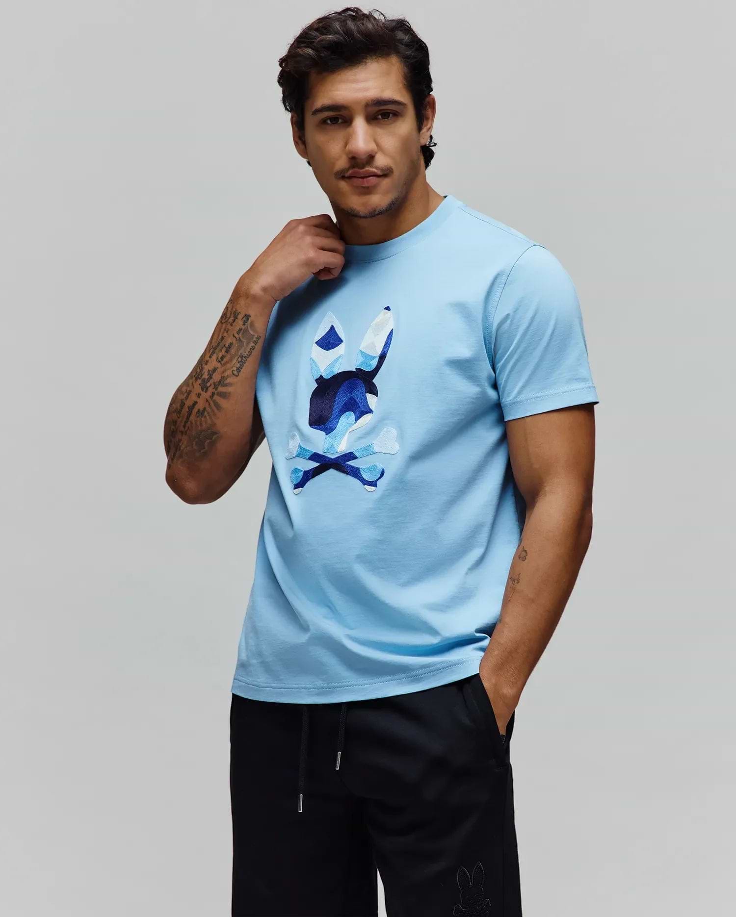 Sky Blue Mens Ara Graphic Tee, a classic fit jersey knit t-shirt featuring a large, multi-tone blue and white geometric Psycho Bunny skull and crossbones graphic on the chest. (2)