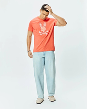 Mens Brad Graphic Tee, a coral classic fit jersey t-shirt featuring a large white patterned Psycho Bunny skull and crossbones graphic on the chest.