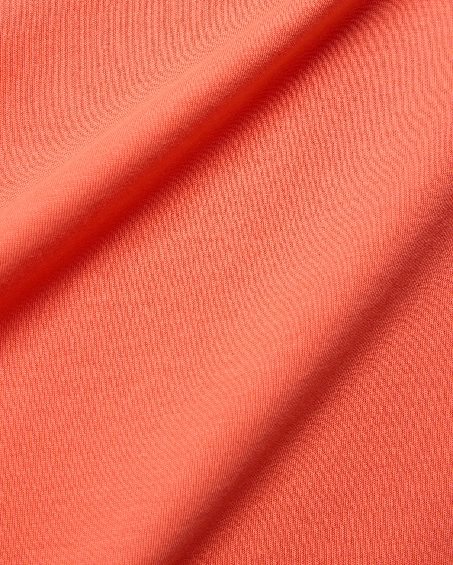 Mens Brad Graphic Tee fabric swatch in a rich, vibrant coral hue, showcasing a soft, finely textured jersey knit, embodying Psycho Bunny's premium menswear and bold color aesthetic.