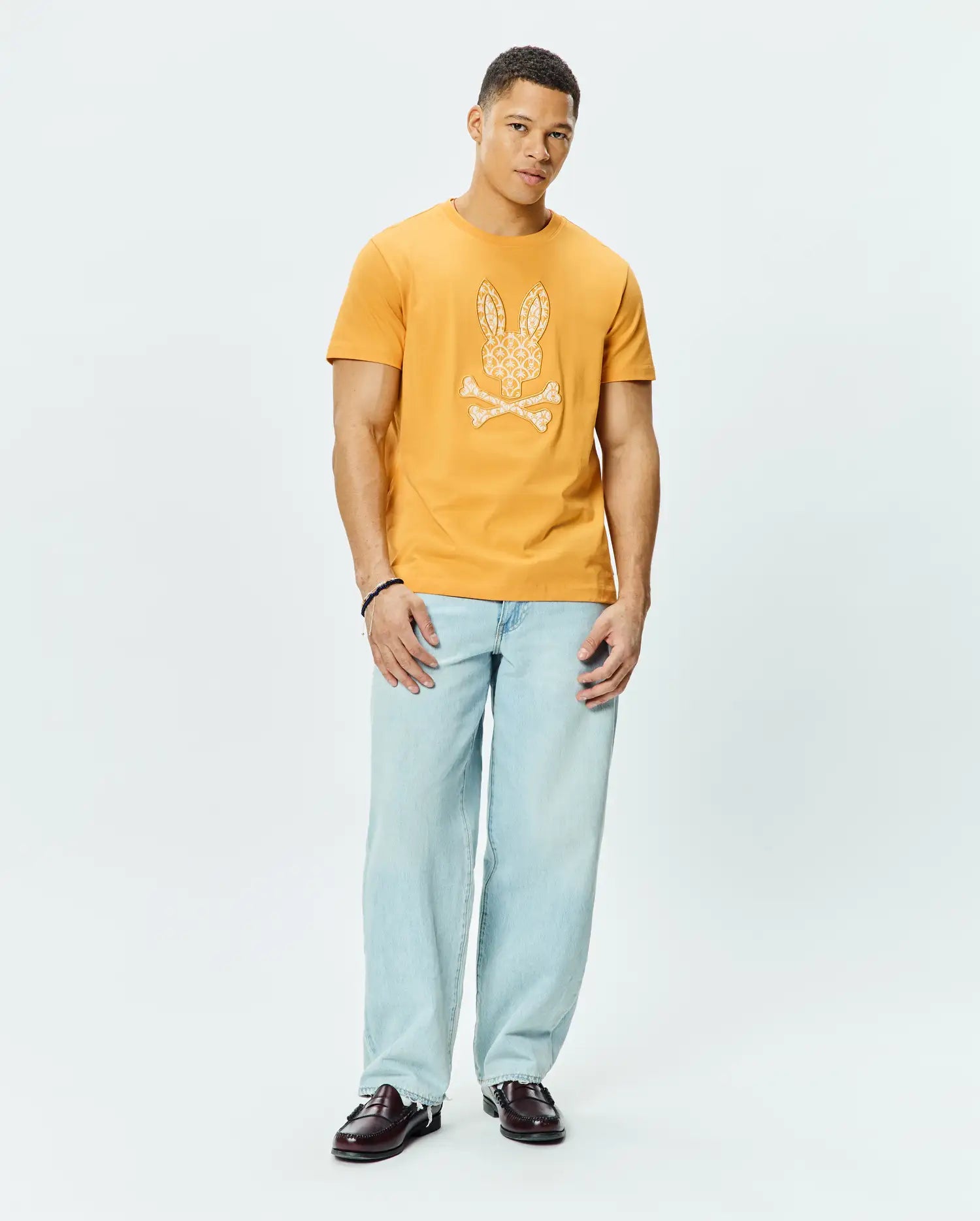 Mens Brad Graphic Tee in mustard yellow, a classic fit soft jersey t-shirt featuring a large white patterned Psycho Bunny skull and crossbones graphic on the chest.