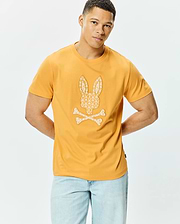 Mens Brad Graphic Tee: Mustard yellow classic fit jersey t-shirt featuring a large central off-white Psycho Bunny skull and crossbones graphic, intricately filled with a repeating mini bunny skull pattern.