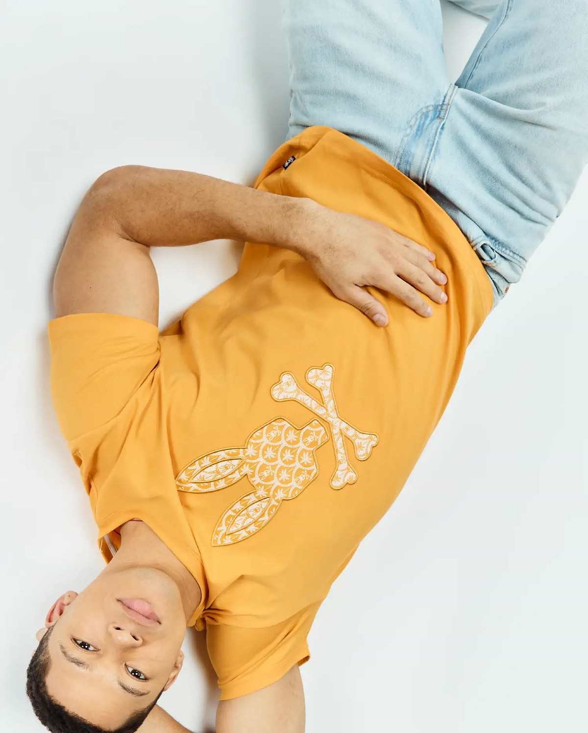 Marigold orange Mens Brad Graphic Tee, classic fit, smooth jersey knit, featuring a large cream and white Psycho Bunny skull logo graphic with intricate floral pattern on the chest.