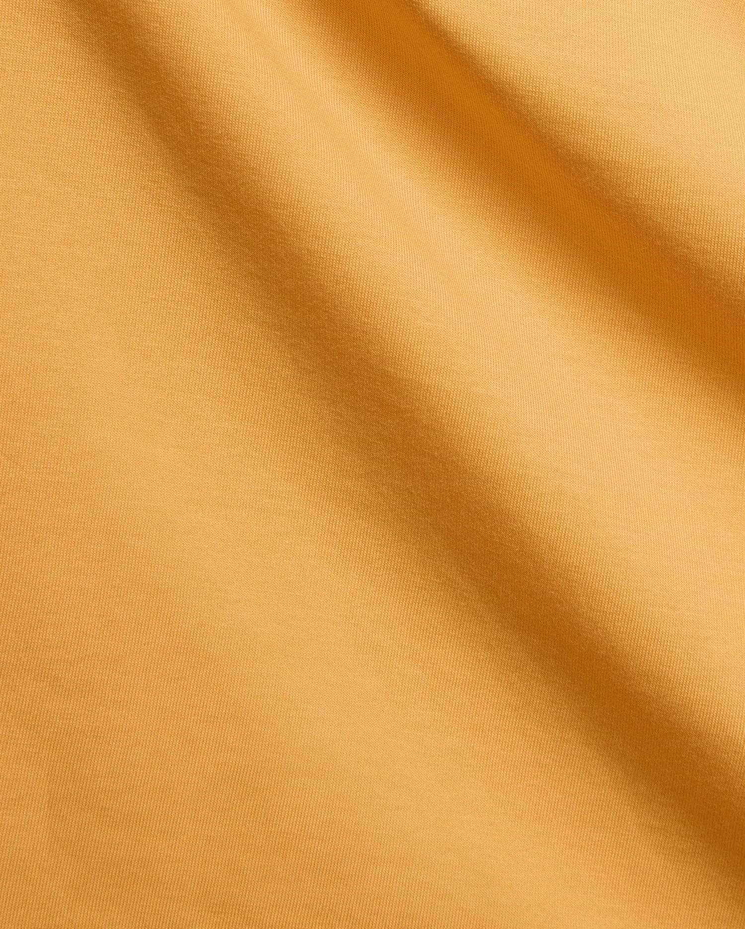 Mens Brad Graphic Tee in vibrant marigold jersey knit fabric with subtle folds, a premium Psycho Bunny streetwear piece featuring an iconic bunny skull logo graphic.