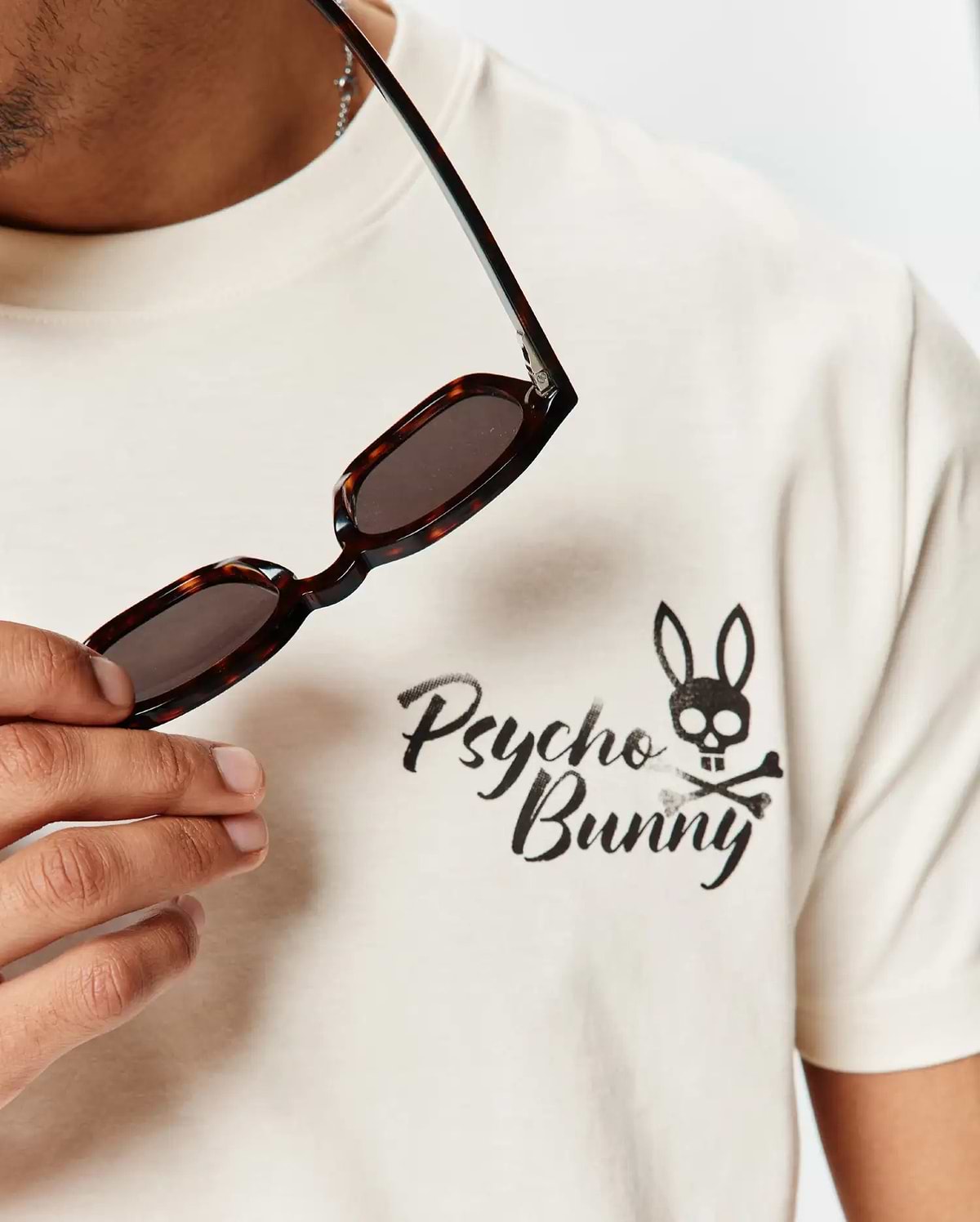 Mens Colin Back Graphic Tee in cream, soft jersey knit, with a front chest graphic: black brushstroke Psycho Bunny text and bunny skull and crossbones logo.