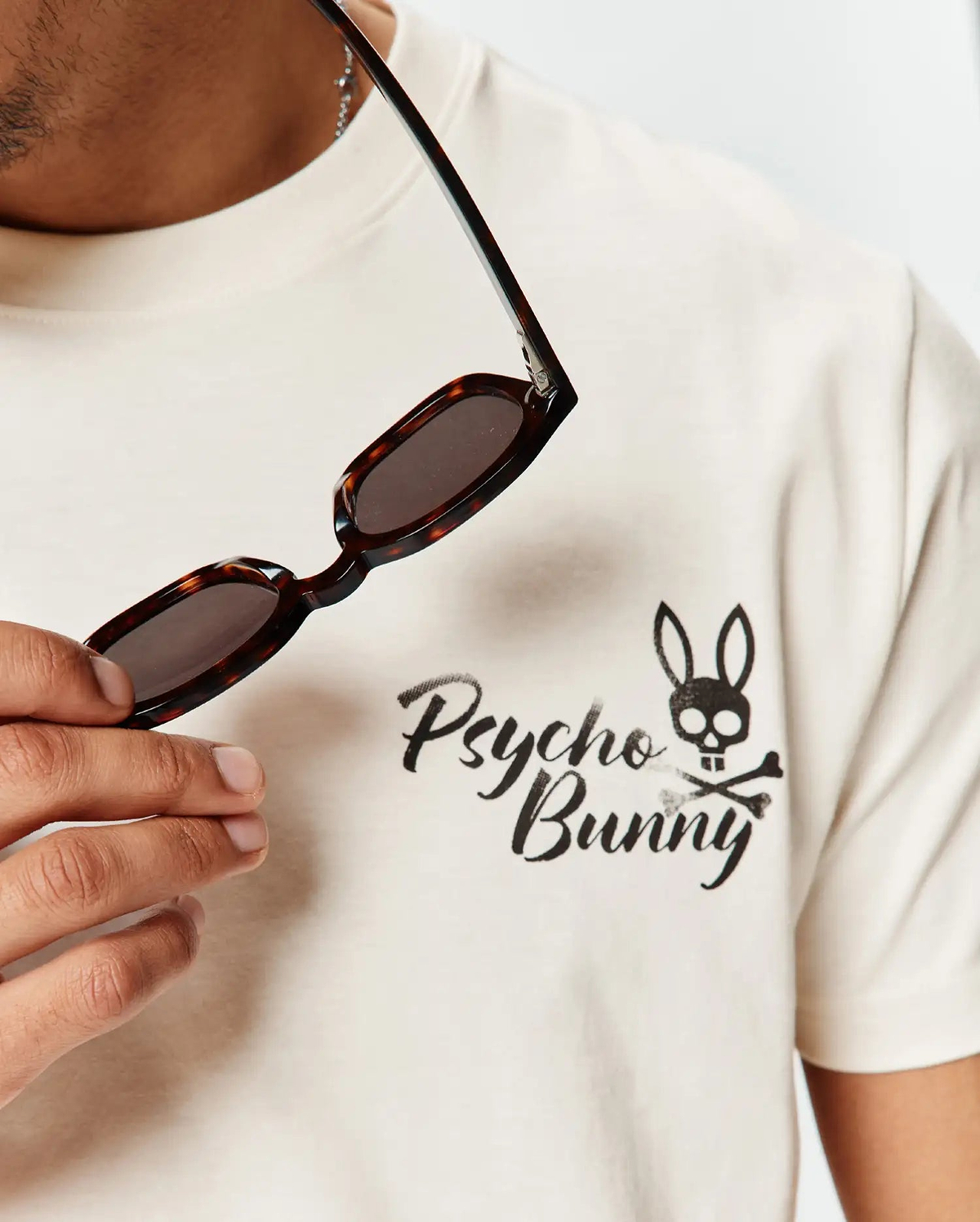 Mens Colin Back Graphic Tee in cream, soft jersey knit, with a front chest graphic: black brushstroke Psycho Bunny text and bunny skull and crossbones logo.