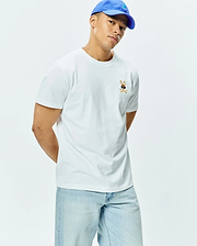 Mens Sunny Chest Graphic Tee, a classic fit white jersey t-shirt featuring a small embroidered brown Psycho Bunny skull logo with blue sunglasses and crossbones on the left chest.