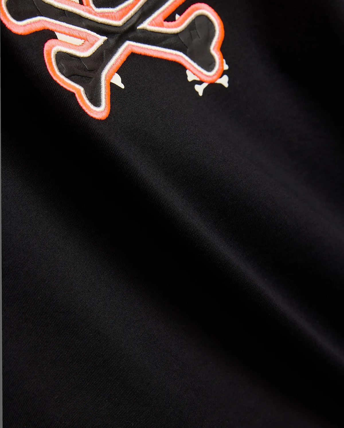 Mens Tanner Bunny Graphic Tee, black jersey knit with a prominent embroidered Psycho Bunny skull logo on the chest, featuring a black skull, white bones, and a vibrant orange outline.