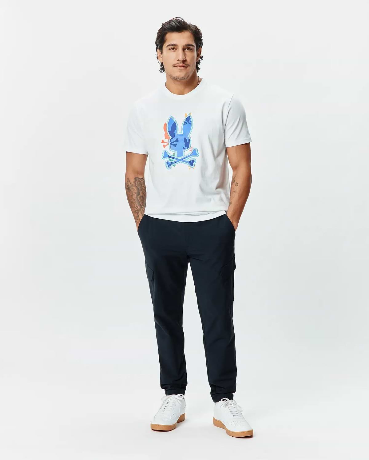 Mens Tanner Bunny Graphic Tee, a classic fit white jersey t-shirt featuring a large, vibrant blue Psycho Bunny skull graphic with orange, yellow, and green accents on the chest, paired with slim navy joggers. (5)