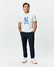 Mens Tanner Bunny Graphic Tee, a classic fit white jersey t-shirt featuring a large, vibrant blue Psycho Bunny skull graphic with orange, yellow, and green accents on the chest, paired with slim navy joggers. (5)