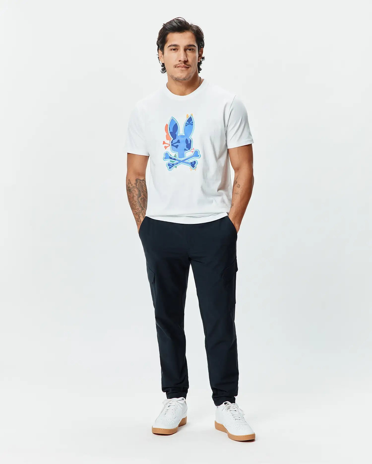 Mens Tanner Bunny Graphic Tee, a classic fit white jersey t-shirt featuring a large, vibrant blue Psycho Bunny skull graphic with orange, yellow, and green accents on the chest, paired with slim navy joggers. (5)