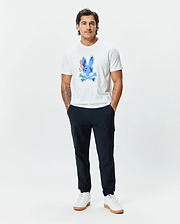 Mens Tanner Bunny Graphic Tee, a classic fit white jersey t-shirt featuring a large, vibrant blue Psycho Bunny skull graphic with orange, yellow, and green accents on the chest, paired with slim navy joggers. (5)