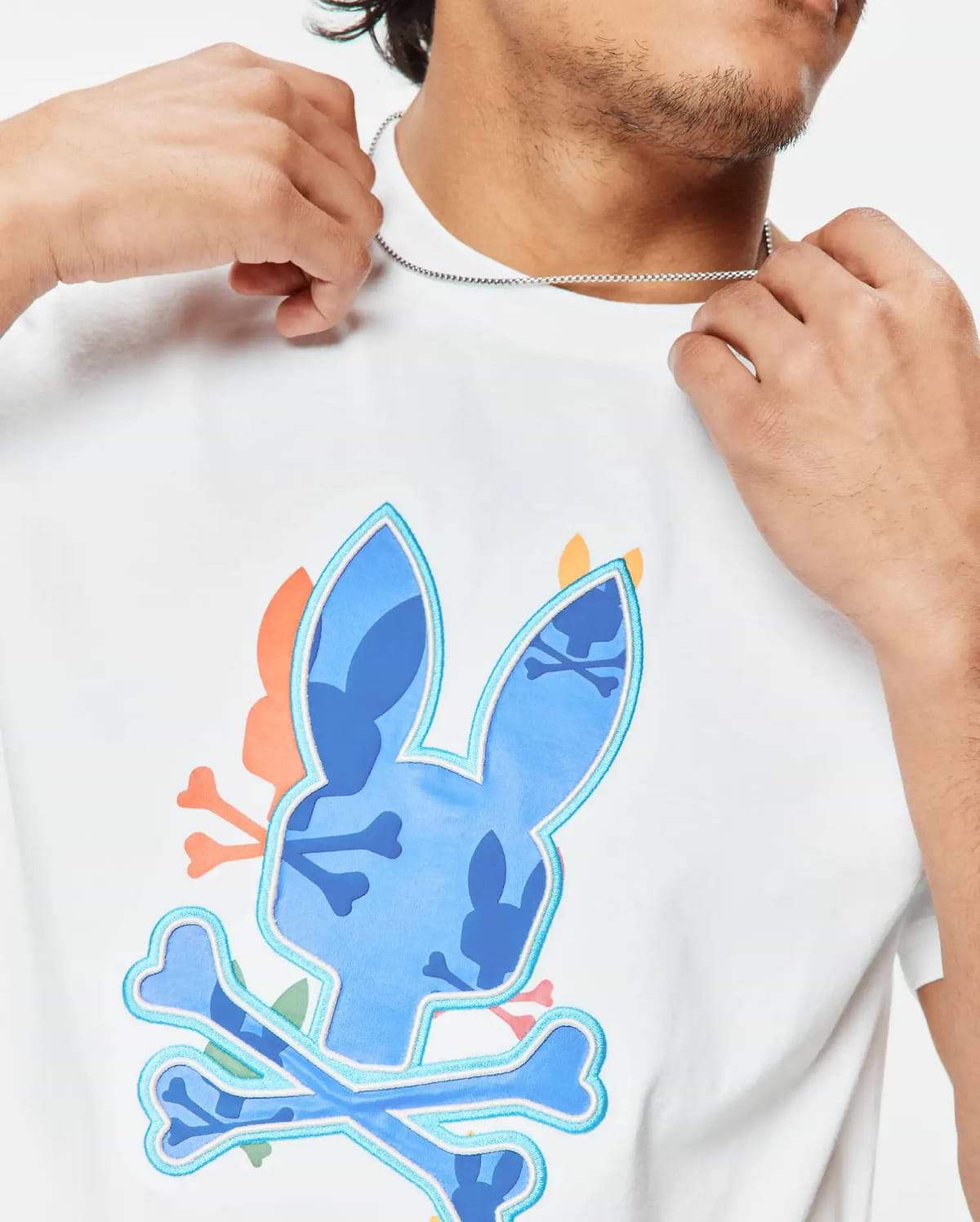 Mens Tanner Bunny Graphic Tee, a white classic fit jersey t-shirt featuring a large central blue camouflage bunny skull logo with light blue outline and crossed bones, accented with orange and pink details. (3)