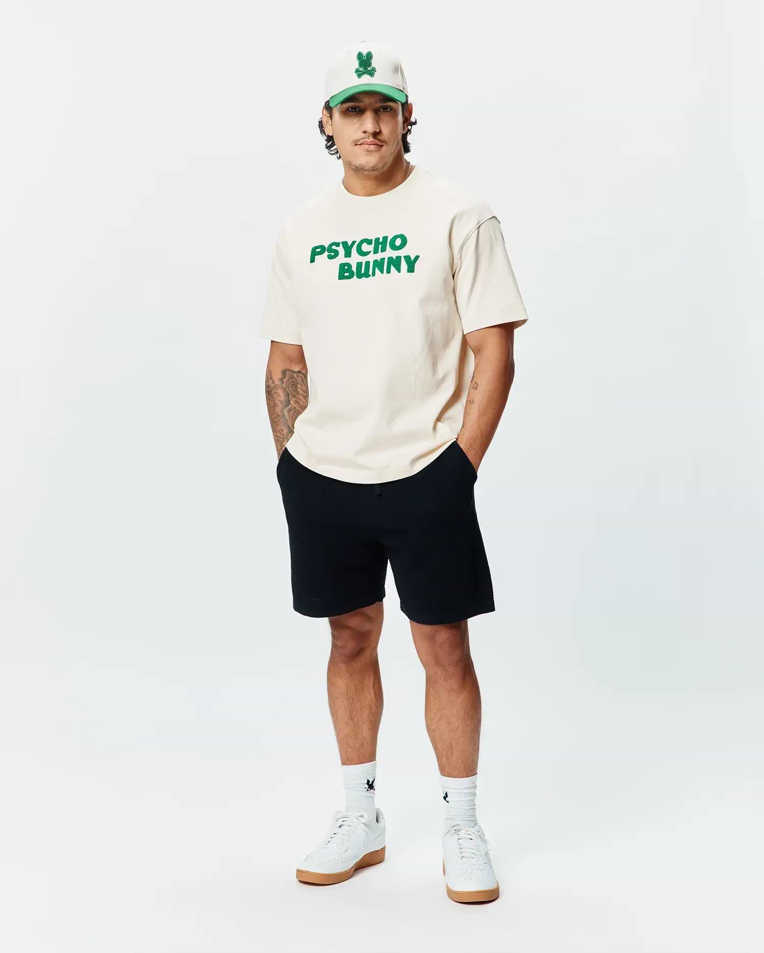Cream Mens Craig Wordmark Tee, a relaxed fit jersey t-shirt featuring a large, bold green PSYCHO BUNNY wordmark graphic prominently displayed on the chest.