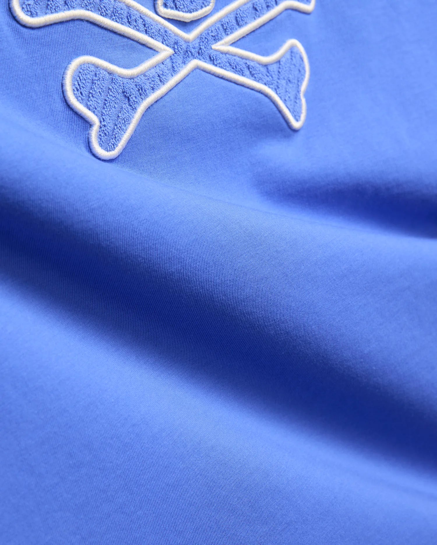 Mens Craig Graphic Tee in vibrant cornflower blue jersey knit, featuring a large, prominent white-outlined terry cloth embroidered crossbones logo. (6)