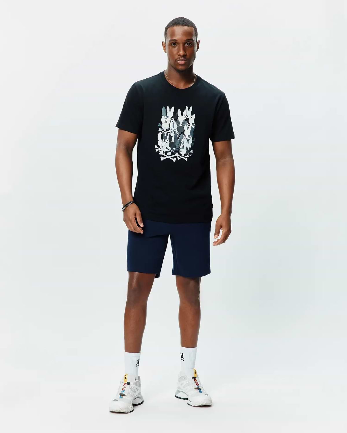 Mens Tanner Graphic Tee, a black classic fit jersey t-shirt featuring a large central chest graphic of multiple white and grey Psycho Bunny skull logos with crossbones.