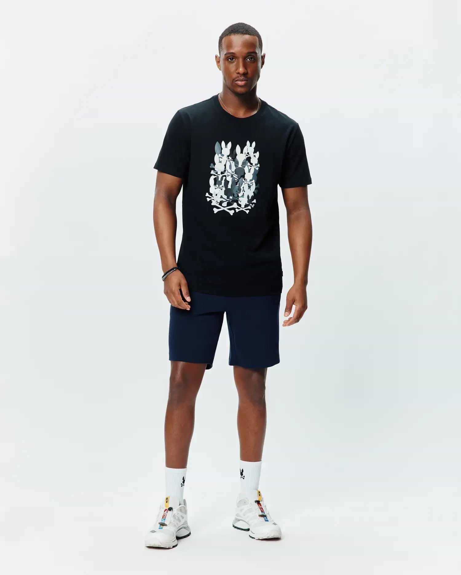 Mens Tanner Graphic Tee, a black classic fit jersey t-shirt featuring a large central chest graphic of multiple white and grey Psycho Bunny skull logos with crossbones.