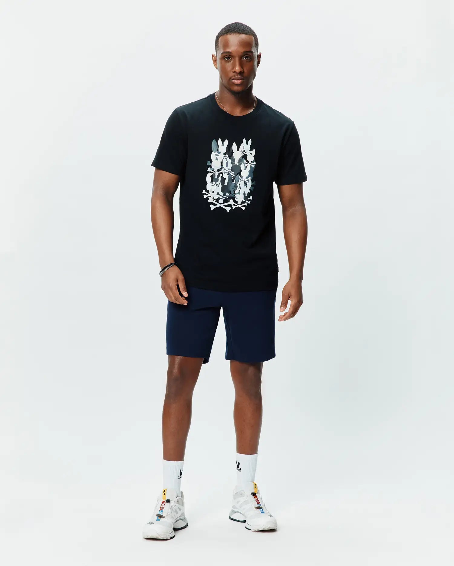 Mens Tanner Graphic Tee, a black classic fit jersey t-shirt featuring a large central chest graphic of multiple white and grey Psycho Bunny skull logos with crossbones.