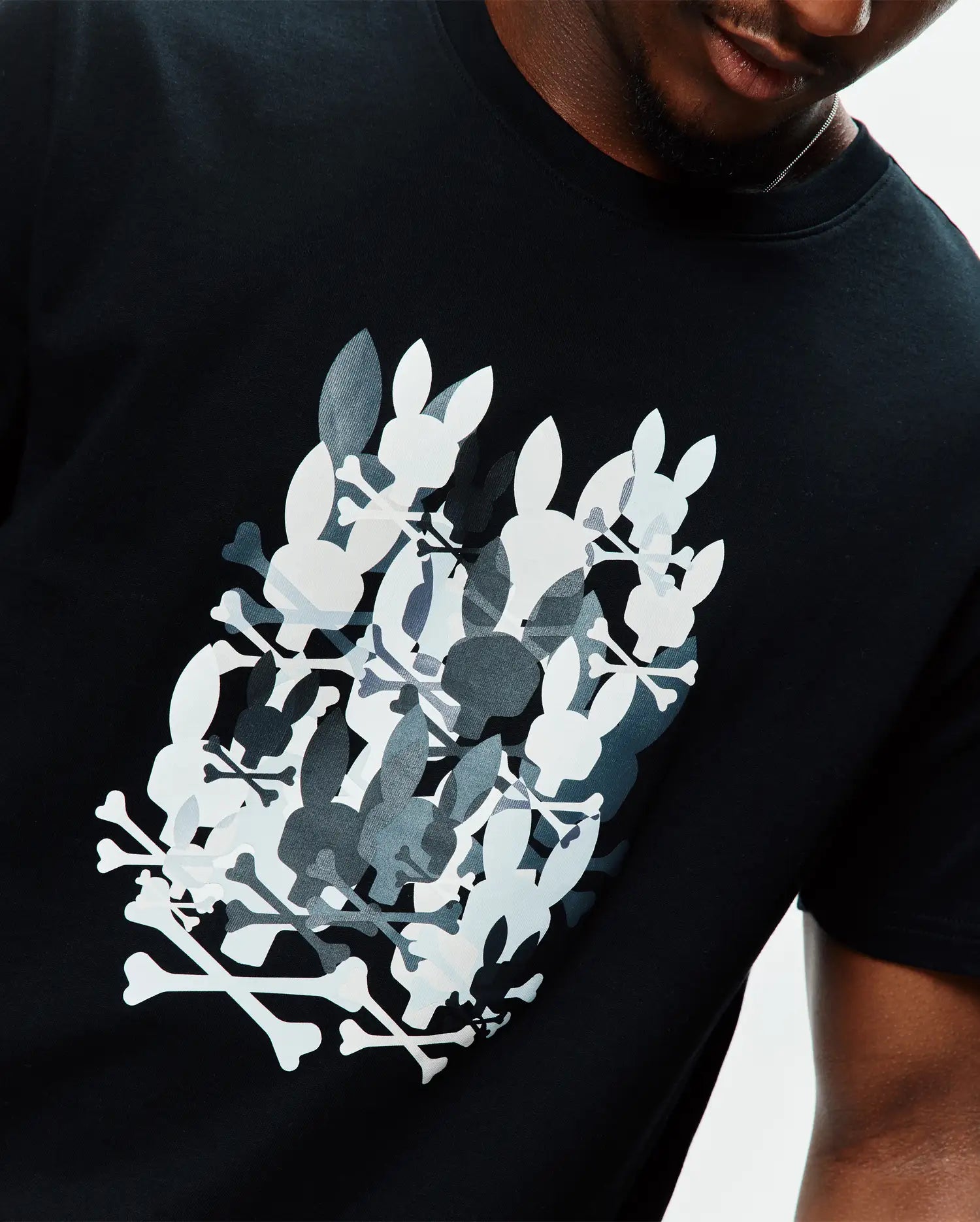 Black Mens Tanner Graphic Tee, classic fit, soft jersey knit, featuring a large chest graphic of overlapping white, grey, and dark grey Psycho Bunny skull and crossbones logos.