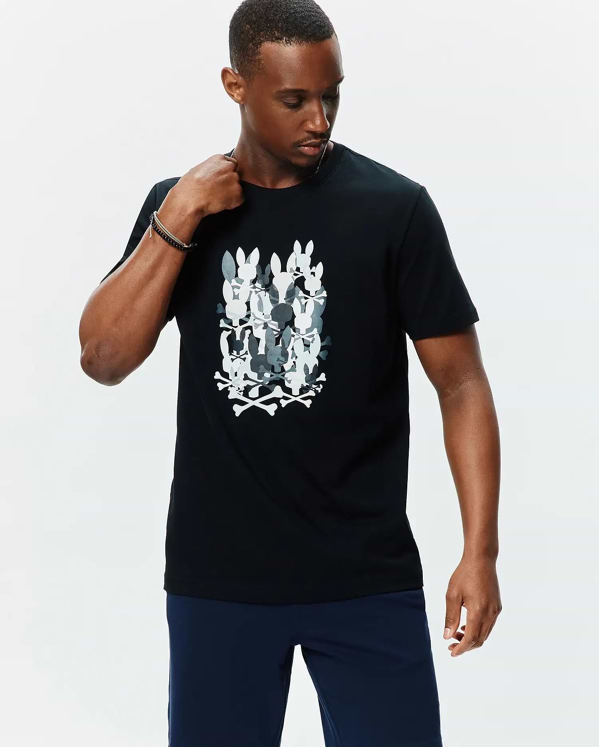 Mens Tanner Graphic Tee, black classic fit jersey t-shirt featuring a large central graphic of stacked white and grey camouflage-patterned Psycho Bunny skull logos with crossbones.