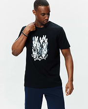 Mens Tanner Graphic Tee, black classic fit jersey t-shirt featuring a large central graphic of stacked white and grey camouflage-patterned Psycho Bunny skull logos with crossbones.